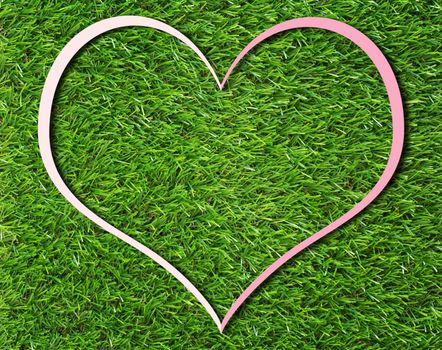 Creative pink heart paper frame on green grass background, love and nature concept