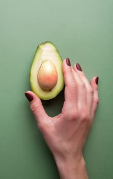 Healthy food concept. Half an avocado in a hand on the green background top view