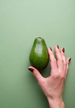 Healthy food concept. Whole avocado in a hand on the green background top view