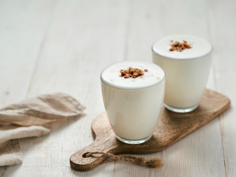 Kefir, buttermilk or yogurt with granola. Yogurt in glass on white wooden background. Probiotic cold fermented dairy drink. Gut health, fermented products, healthy gut flora concept. Copy space