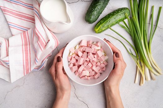 Step by step preparation of cold okroshka soup with sausage, step 4 - adding sliced sausages to the bowl, top view, selective focus