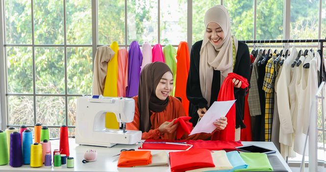 Small business of Muslim woman fashion designer Working and  using smart phone and tablet With Dresses at clothing store