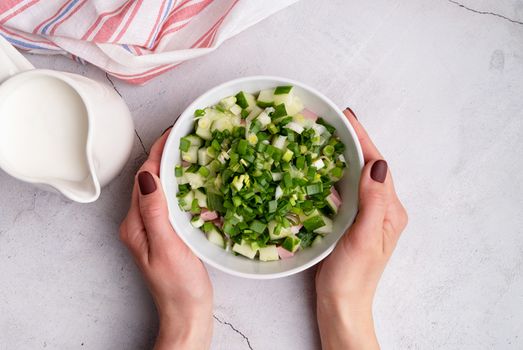 Step by step preparation of cold okroshka soup with sausage, step 6 - adding chopped green onion to the bowl, top view, selective focus