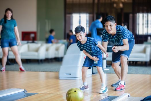 Father teaching son and family play bowling at bowling club on relax time, family activity on holiday concept