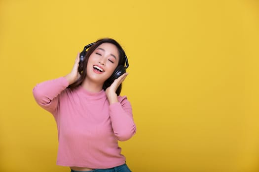 Happy cheerful Beautiful Asian woman wearing wireless headphones enjoying listening to music on yellow background.People lifestyle concept