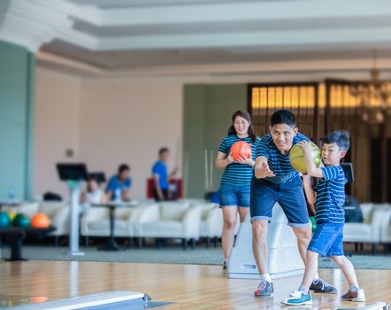 Father teaching son and family play bowling at bowling club on relax time, family activity on holiday concept