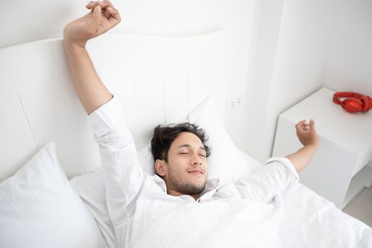 A man waking up in her bed fully rested and open the curtains in the morning to get fresh air.