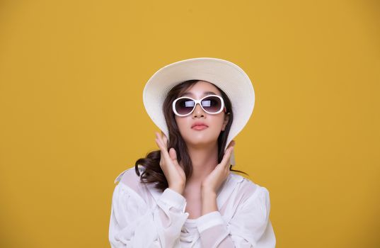 Portrait Asian beautiful happy young woman with sunglasses and hat smiling cheerful in summer and looking at camera isolated on yellow studio background.