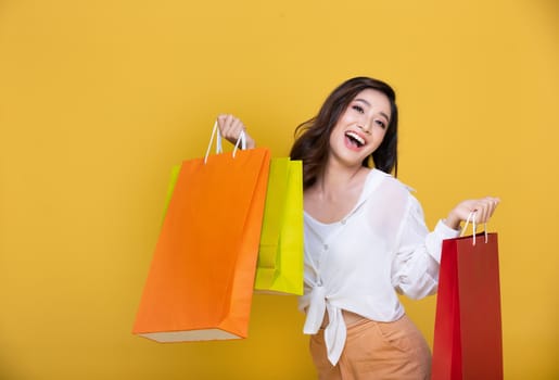 Portrait Asian beautiful happy young woman smiling cheerful and holding shopping bags on yellow background.Happiness, consumerism, sale and people shopping concept
