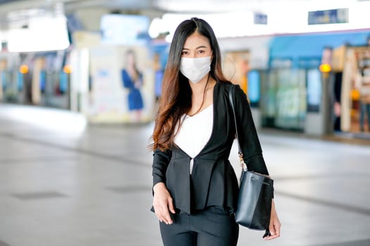 Portrait of business woman with hygiene mask stand in the station of sky train. She still go to work during Covid-19 pandemic in the city.
