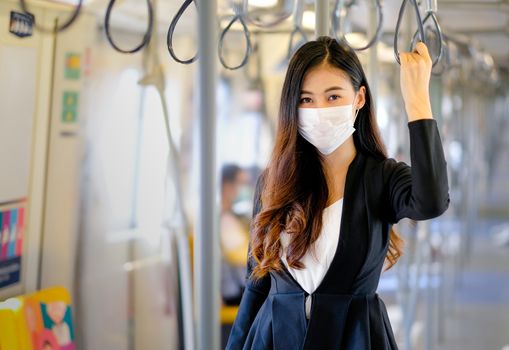Portrait of beautiful business woman with hygiene mask stand with hold handrail in sky train along the way for working during coronavirus spreading in city.