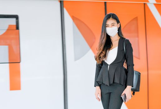 Portrait of pretty woman with mask stand in front of door of sky train on the platform during coronavirus pandemic in city.