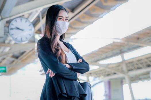 Business girl with hygiene mask stand on platform for waiting the sky train during go to work in situation of coronavirus pandemic in city.