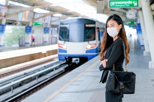 Beautiful business woman with hygiene mask stand in front of sky train wait for going to work during Covid-19 pandemic in the city.