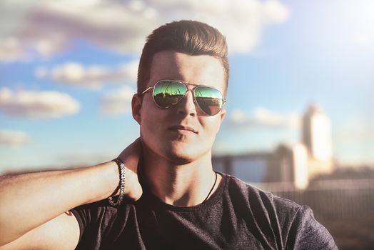 Portrait of a handsome stylish guy in sunglasses who poses outdoors