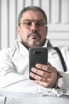 The bad news. A seriously displeased businessman in a white shirt is looking on the phone. foreground focus