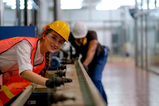 Beautiful worker or technician or engineer woman smile and look forward in front of rail of the machine with her co-worker as background in factory.