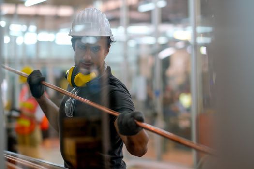 Technician or worker man hold copper pipe and look through glass window in the factory.