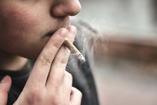 Guy smokes a cigarette outside, portrait, close-up, smoke