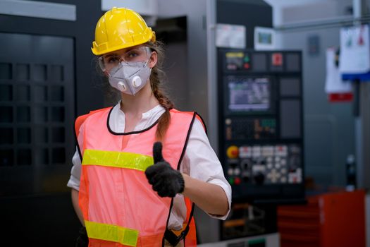 Factory woman worker or technician with mask stand with confident action in front of machine and show thumbs up.