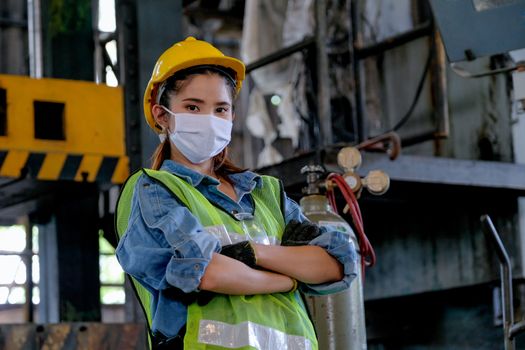Factory woman worker or technician with hygienic mask stand with confident action with big machine as background.