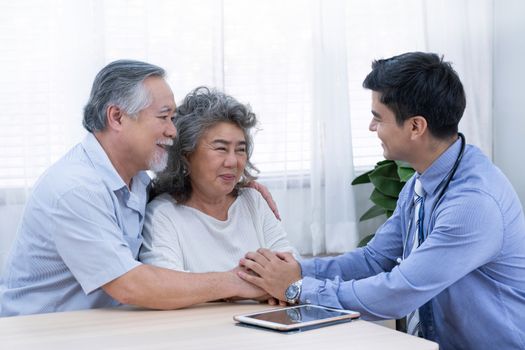 The doctor with blue shirt and stethoscope encourage old man by holding their hands and woman about their health during a visit home for check-up elder people at home for elderly good healthcare.