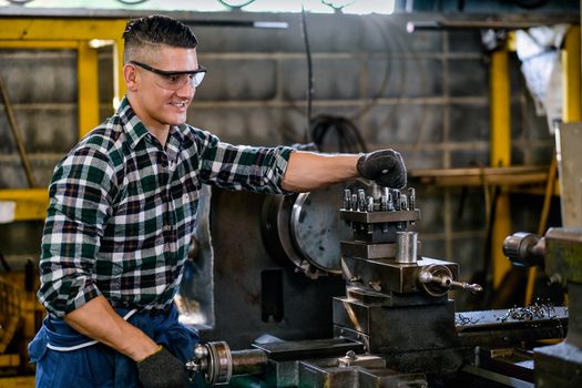 Smart technician or engineer worker man with protective eye glasses work with machine and look happy in factory workplace. Concept of good system of management to get better industrial business.