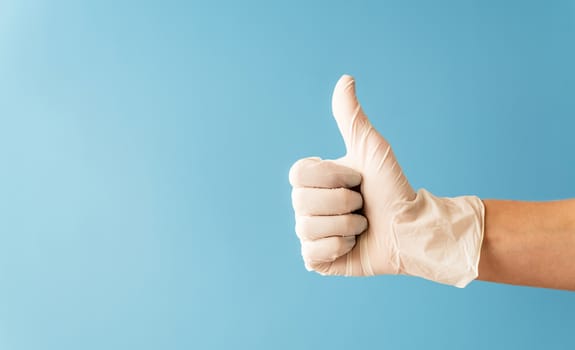 Hand wearing white rubber glove giving the thumbs up signal on blue background