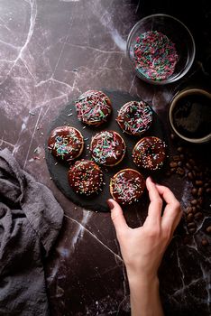 Fresh donuts with chocolate glaze and colorful sprinkles on dark background, top view