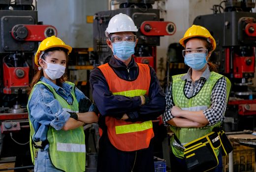 Group of man and woman workers with mask stand with confident action in the factory workplace and various machine as background.