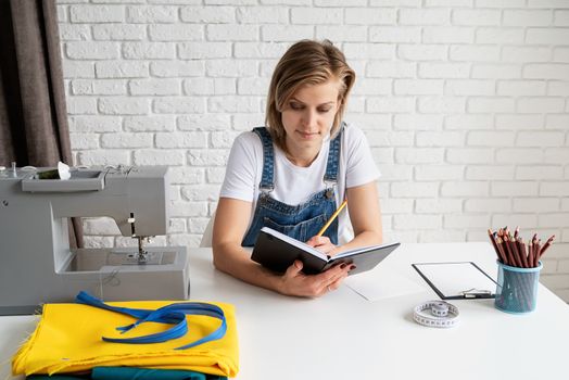 Young blond tailor or designer drawing a sketch for new clothes