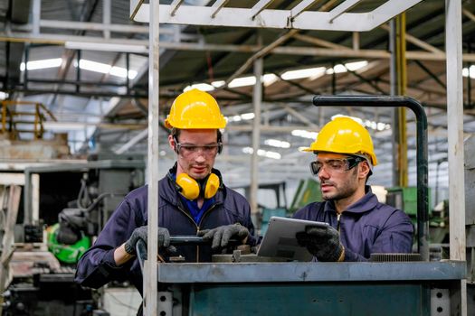 Two technician men with blue uniform and yellow helmet work with the machine in factory.