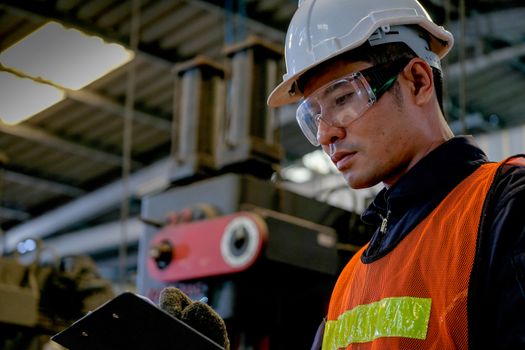 Close up Asian worker or technician man write on document paper in factory in front of machine.  Concept of good system and manager support for better industrial business.