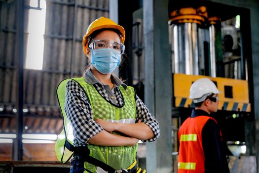 Factory woman worker or technician with hygienic mask stand with confident action with her co-worker engineer in workplace during concern about corona pandemic in people affect industrial business.