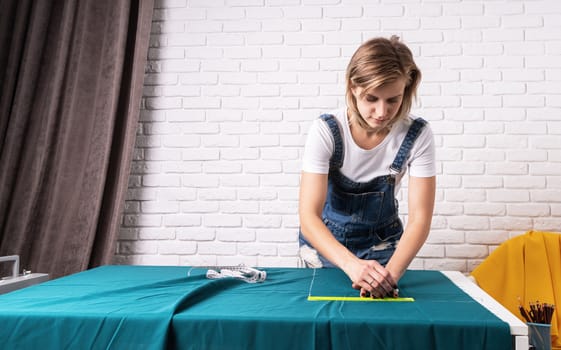 Young woman sewing clothes. Woman tailor working with textile in her studio