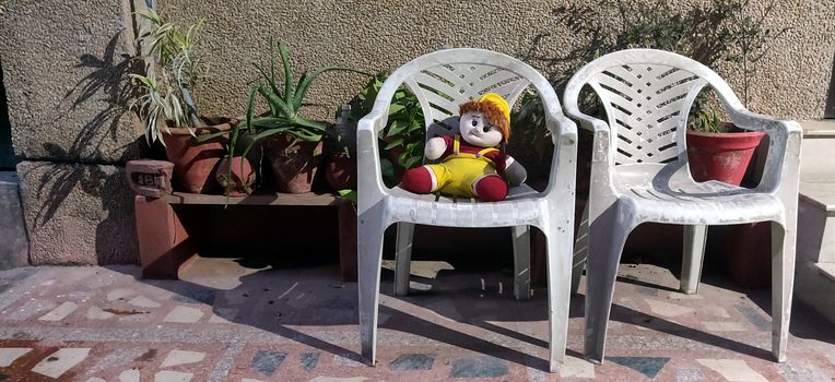 A stuffed doll sitting on a plastic chair alone in backyard in India during summer in lock down of corona virus period 2020