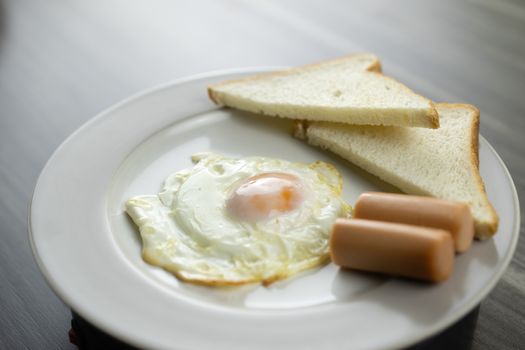 Close-up of breakfast on a white plate in the bottom right corner of the wooden floor