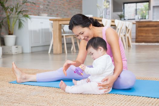 Happy mother and baby daughter sitting on exercising mat at home