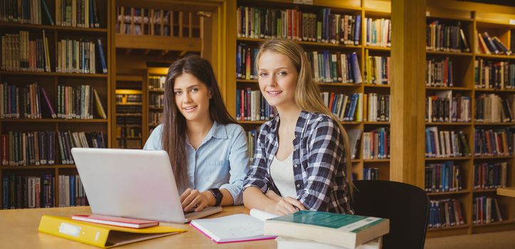 Smiling students using laptop in library 