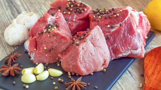 Red meat on a black Board sprinkled with pepper, garlic, anise and lime. Billets for barbecue,  steak or shish kebabs. Cooking for lunch the fresh diet of red meat for gourmets.