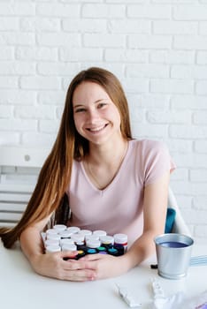 smiling young female artist holding a pile of paint bottles working in her studio