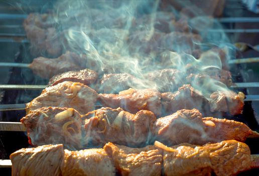 Meat on grill. Morning BBQ. Cooking barbecue on the grill with smoke. Cook fresh marinated meat with onions. Grill marinated barbecue is prepared on the grill on the coals