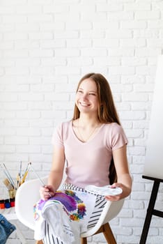 smiling young female artist holding a color palette and paintbrush working in her studio