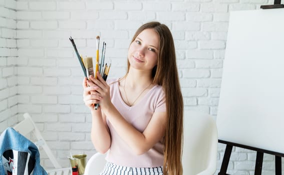 smiling young female artist holding paintbrush working in her studio