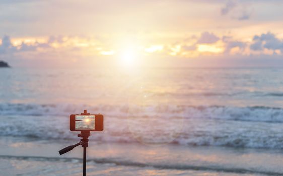 Someone travel at Patong beach, Phuket, Thailand keep mobile phone on tripot wait time sunset for good photo. selective focus on mobile phone and soft focus the sea and sky