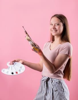Female artist with a color palette and paintbrushes isolated on pink background