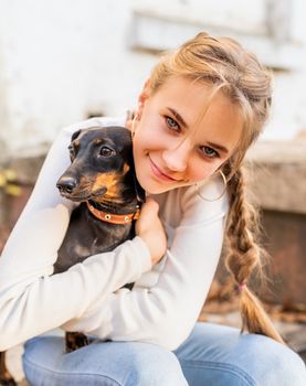 Pet care concept. Young woman hugging her dachshund dog outdoors. Focus on woman face