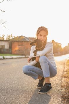 Pet care concept. Young woman with plaited hair hugging her dachshund dog outdoors in sunset