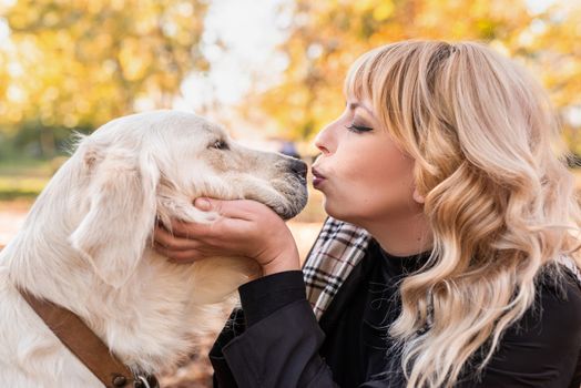 Pet care concept. Happy blond woman kissing her retriever dog in autumn park