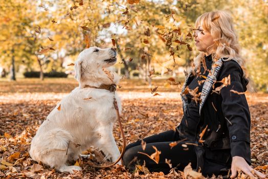 Pet care concept. Happy blond woman playing with her retriever dog in autumn park